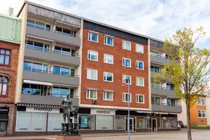 Flerbostadshus med röd tegelfasad, vita och röda fönster, kommersiella lokaler på första våningen | Nivika Fastigheter AB (publ)