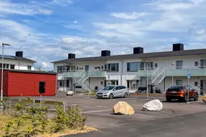Flerbostadsfastighet med vit träfasad, svart tak och röda förråd | Nivika Fastigheter AB (publ)