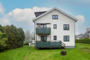 Flerbostadshus med vit fasad, svarta fönster och mörkgrön trappa | Nivika Fastigheter AB (publ)