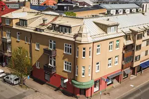 Flerbostadshus med röd och orange putsad fasad, vita fönster, ljust plåttak | Nivika Fastigheter AB (publ)