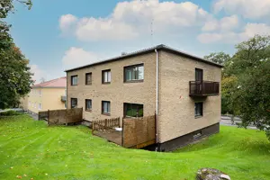 Flerbostadshus med beige tegelfasad, bruna fönster, terrasser av trä på baksidan | Nivika Fastigheter AB (publ)