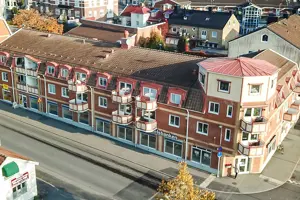 Flerbostadshus med röd tegelfasad, vita fönster och rött tak, bild tagen ovanifrån | Nivika Fastigheter AB (publ)