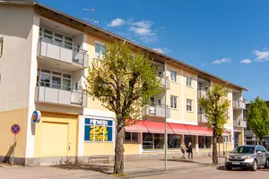 Flerbostadshus med vit och gul fasad, vita fönster och en röd markis | Nivika Fastigheter AB (publ)