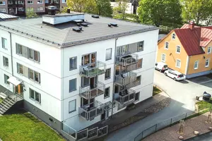 Flerbostadshus med vit fasad, mörkgrå fönster samt mörkgrå husgrund | Nivika Fastigheter AB (publ)